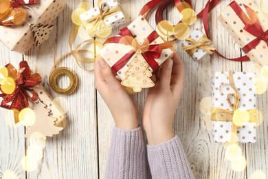 Woman holding Christmas gift box with red bow at wooden table, top view