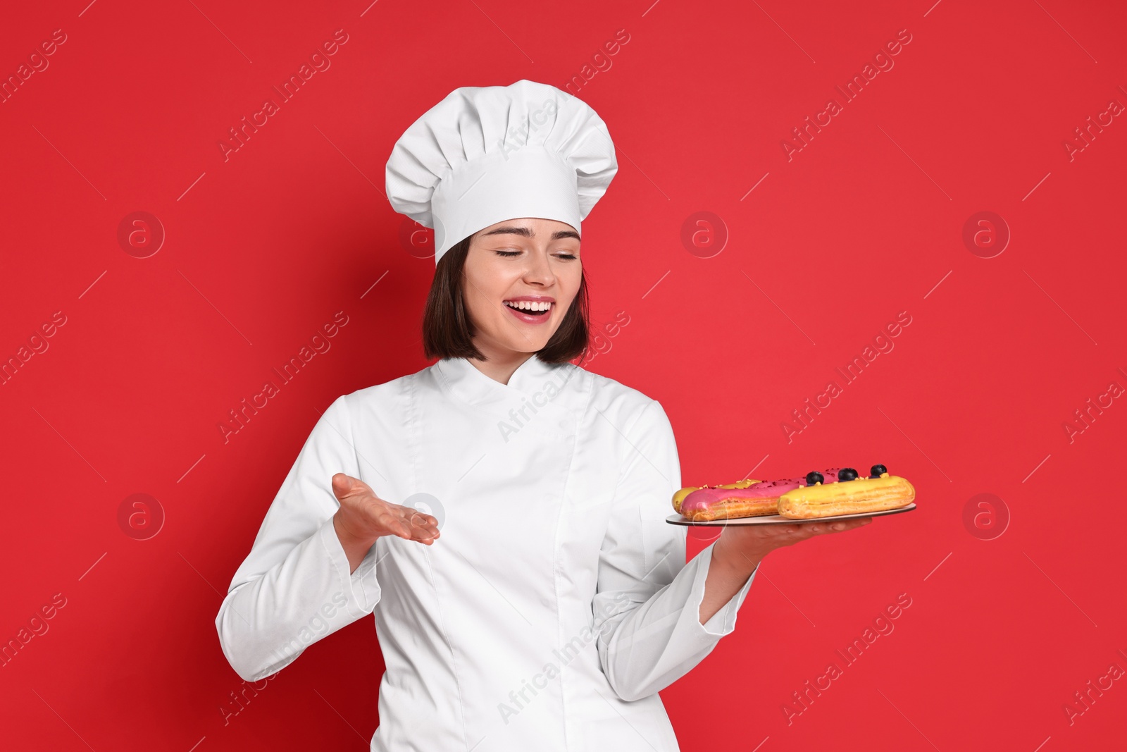 Photo of Happy confectioner with delicious eclairs on red background