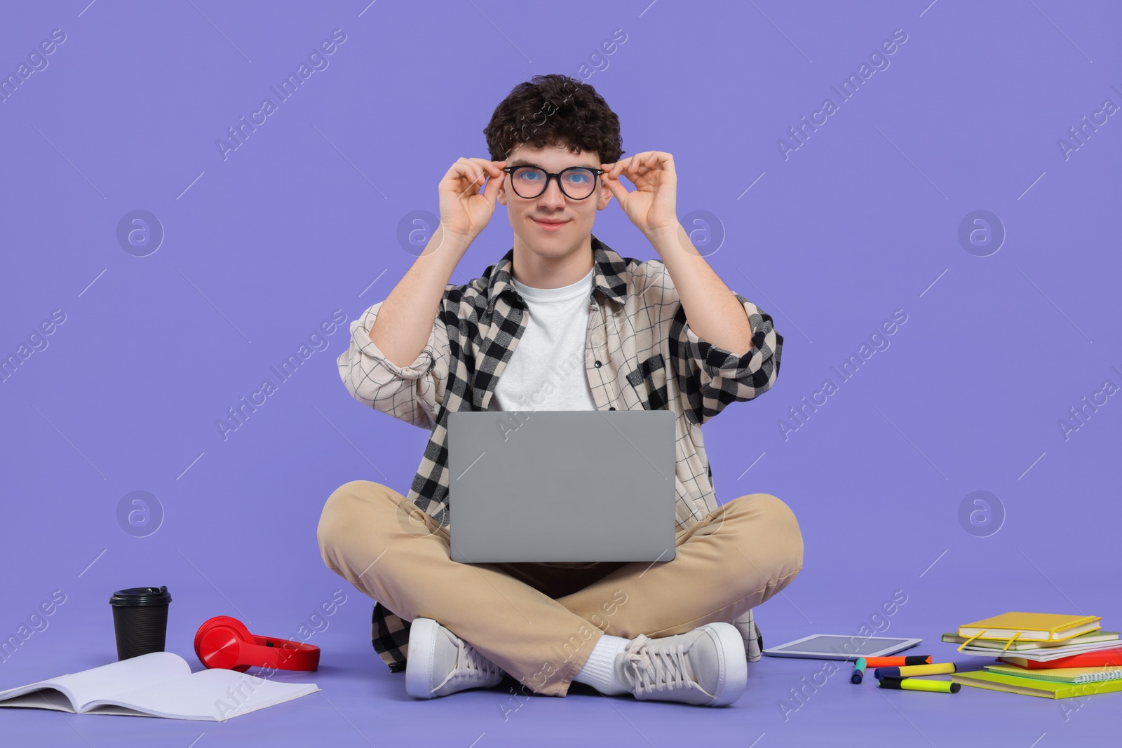 Photo of Portrait of student with laptop and stationery sitting on purple background