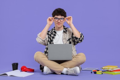 Portrait of student with laptop and stationery sitting on purple background