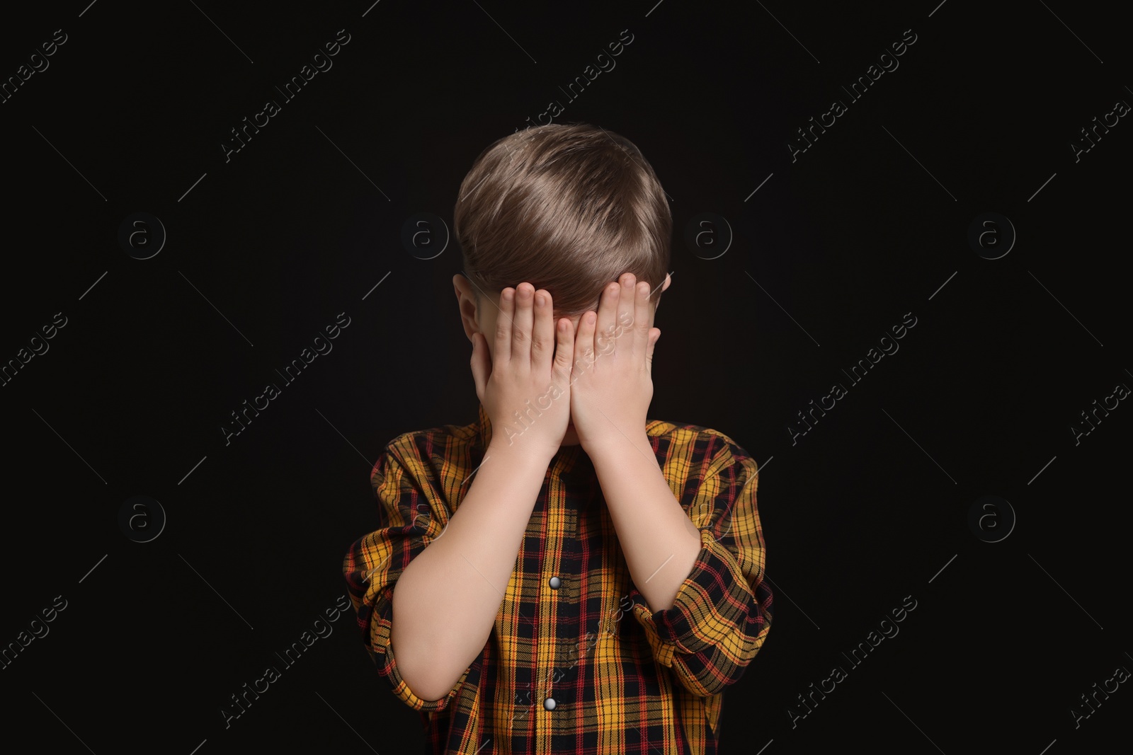 Photo of Boy covering face with hands on black background. Children's bullying