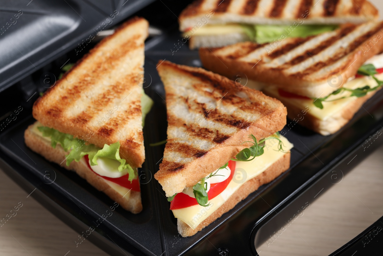 Photo of Modern grill maker with sandwiches on table, closeup view