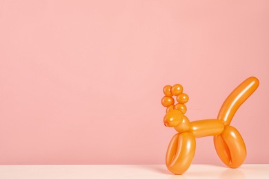 Photo of Animal figure made of modelling balloon on table against color background. Space for text