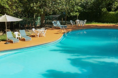 Photo of Pool with clean water, sunbeds and parasol outdoors