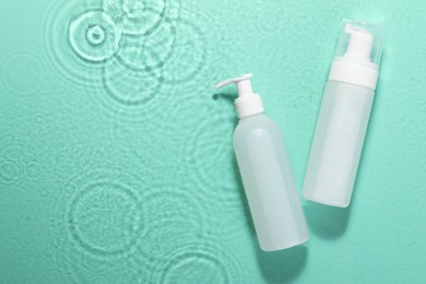 Bottles of face cleansing product on water against turquoise background, flat lay. Space for text