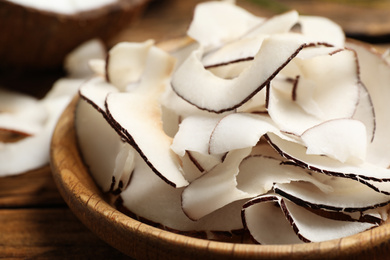 Photo of Tasty coconut chips in wooden plate, closeup