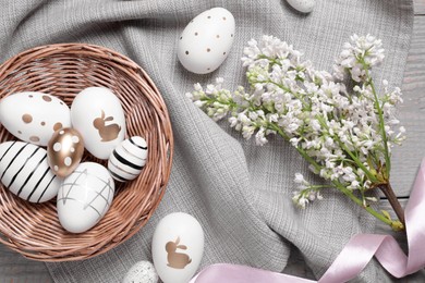Many painted Easter eggs, branch with lilac flowers and ribbon on grey wooden table, flat lay