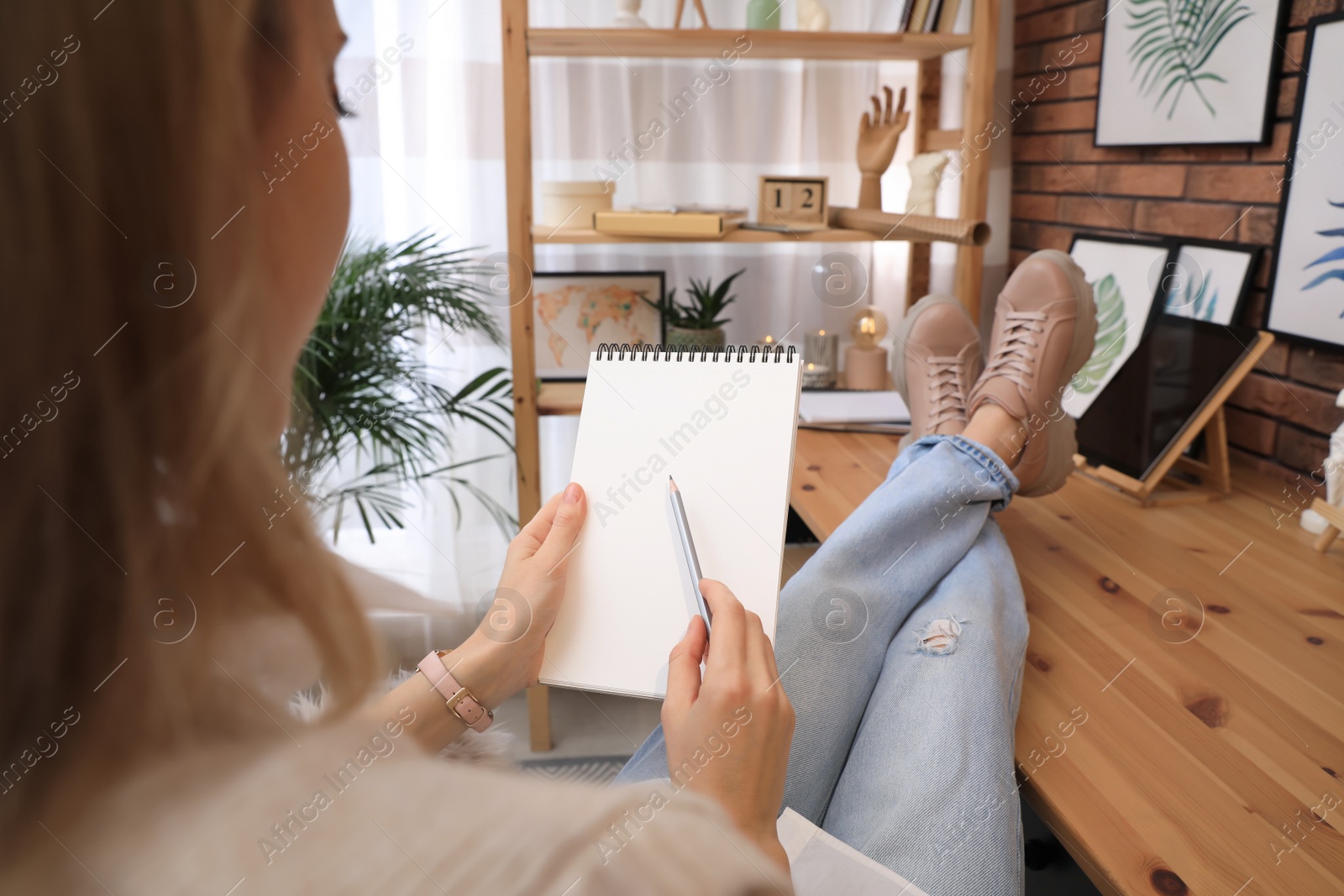 Photo of Woman drawing in sketchbook with pencil at home, closeup