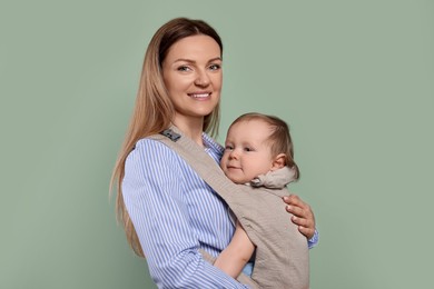 Photo of Mother holding her child in sling (baby carrier) on olive background