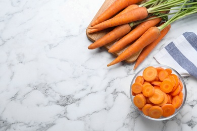 Whole and cut ripe carrots on white marble table, flat lay. Space for text