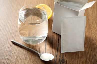 Medicine sachets, glass of water, spoon and lemon on wooden table