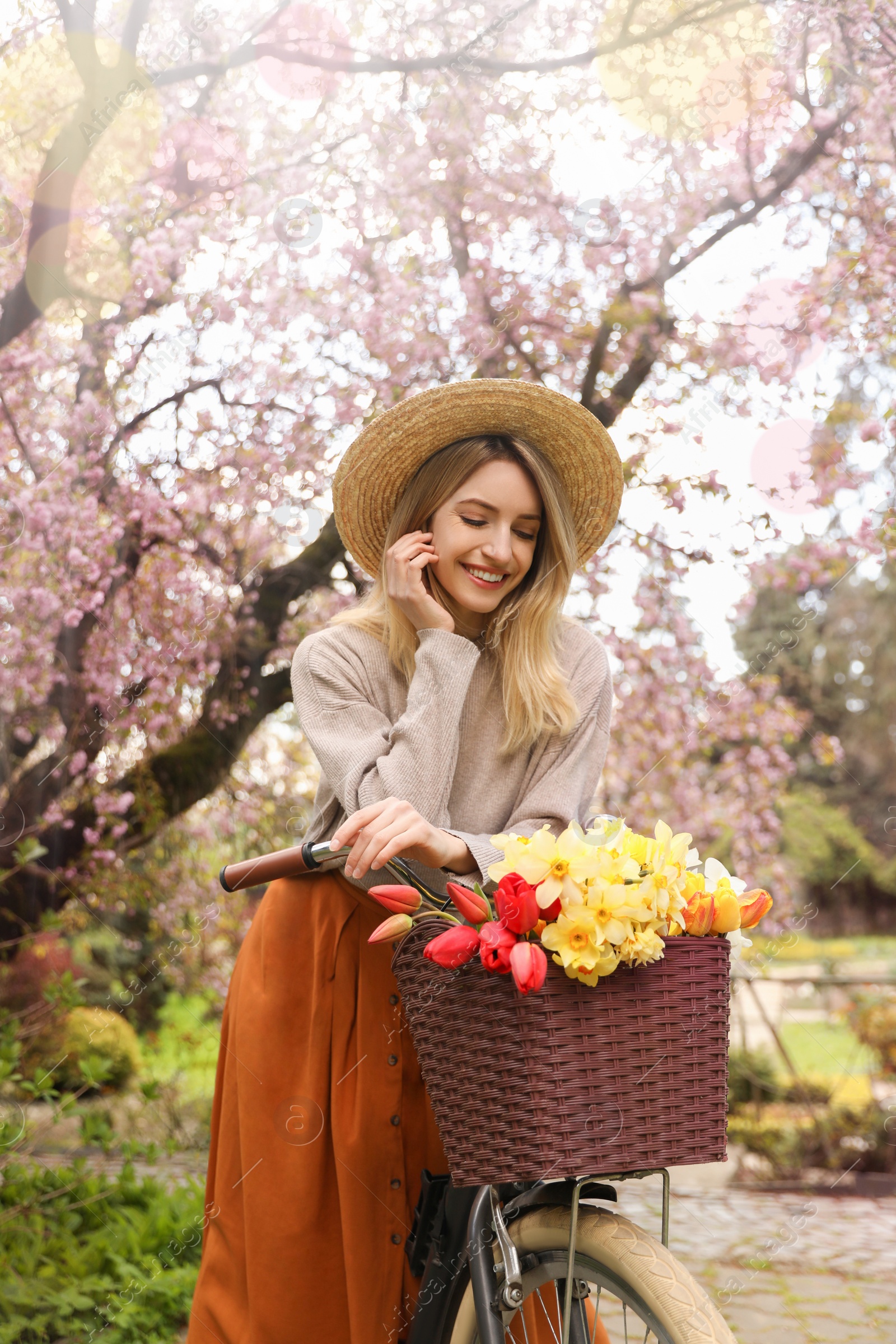 Photo of Beautiful young woman with bicycle and flowers in park on pleasant spring day