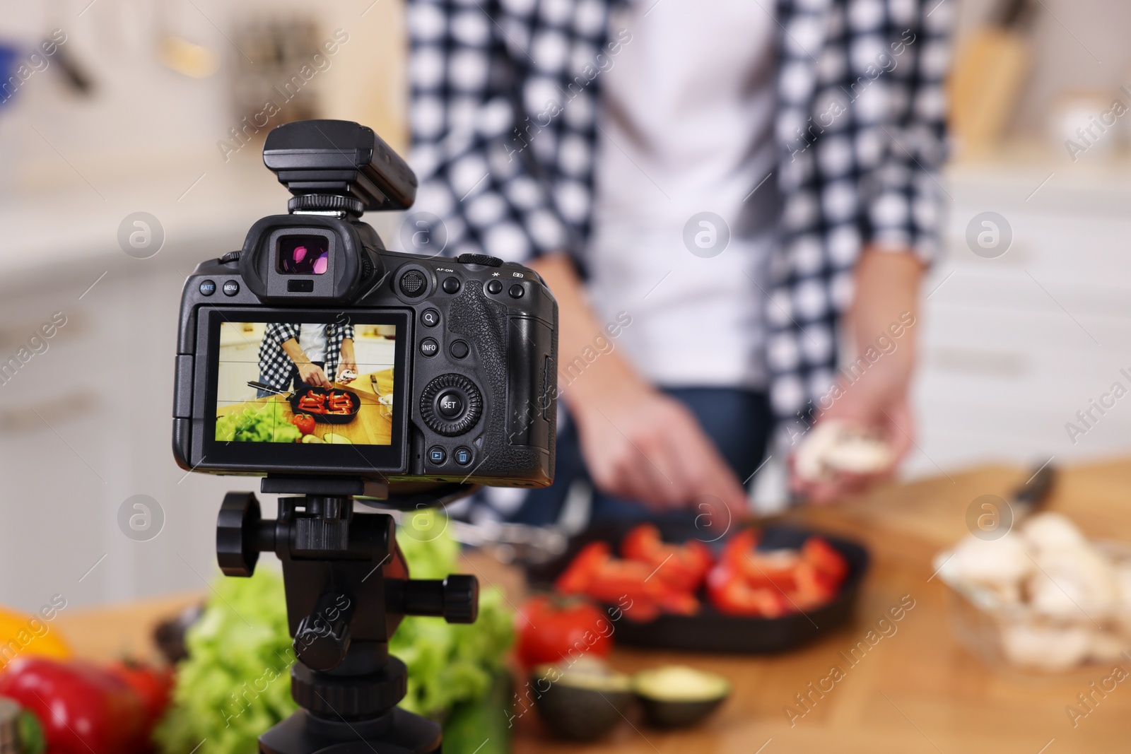 Photo of Food blogger cooking while recording video in kitchen, focus on camera