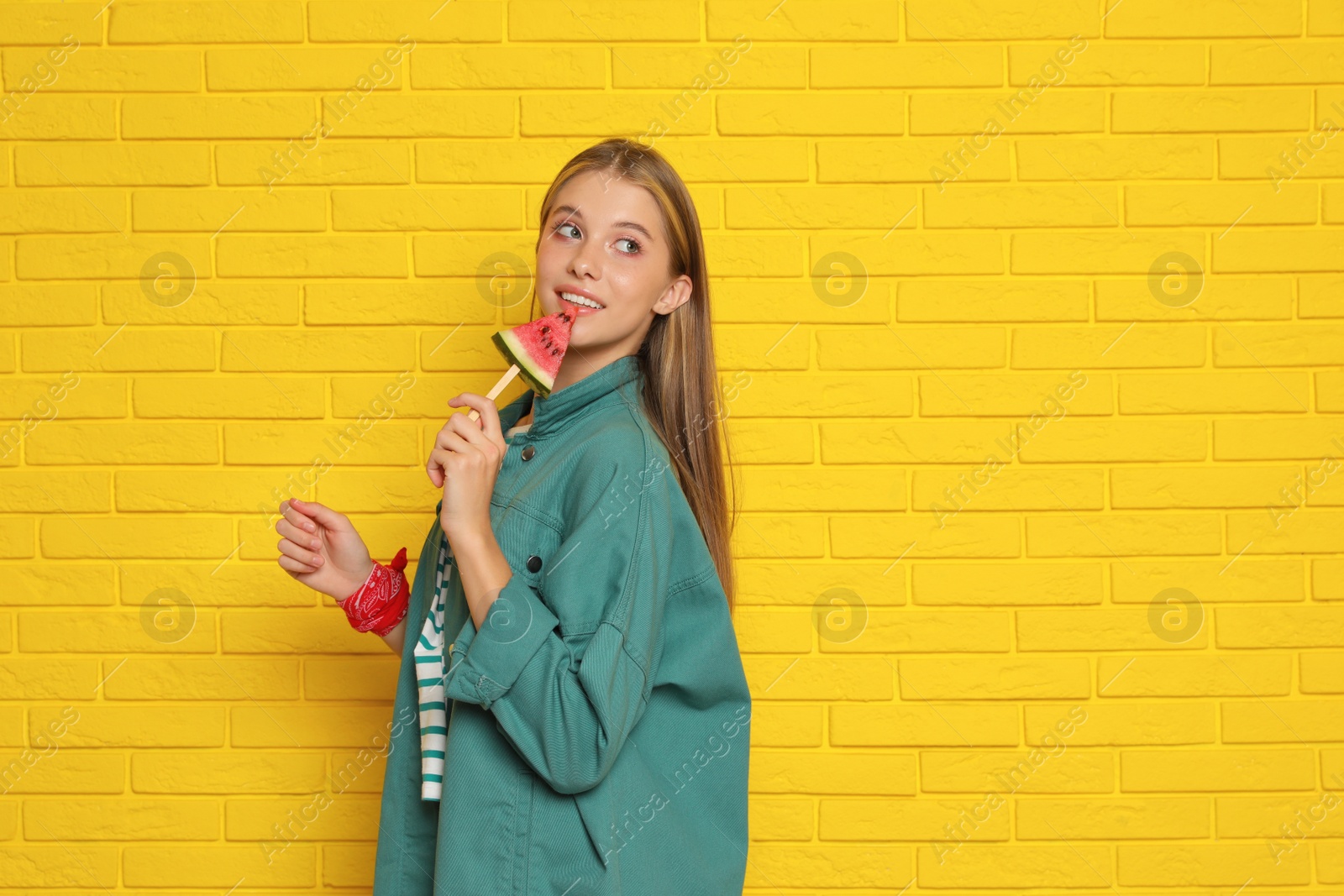 Photo of Beautiful girl with piece of watermelon near yellow brick wall. Space for text