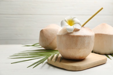 Photo of Young peeled coconuts with straw, palm leaf and flower on white wooden table. Space for text
