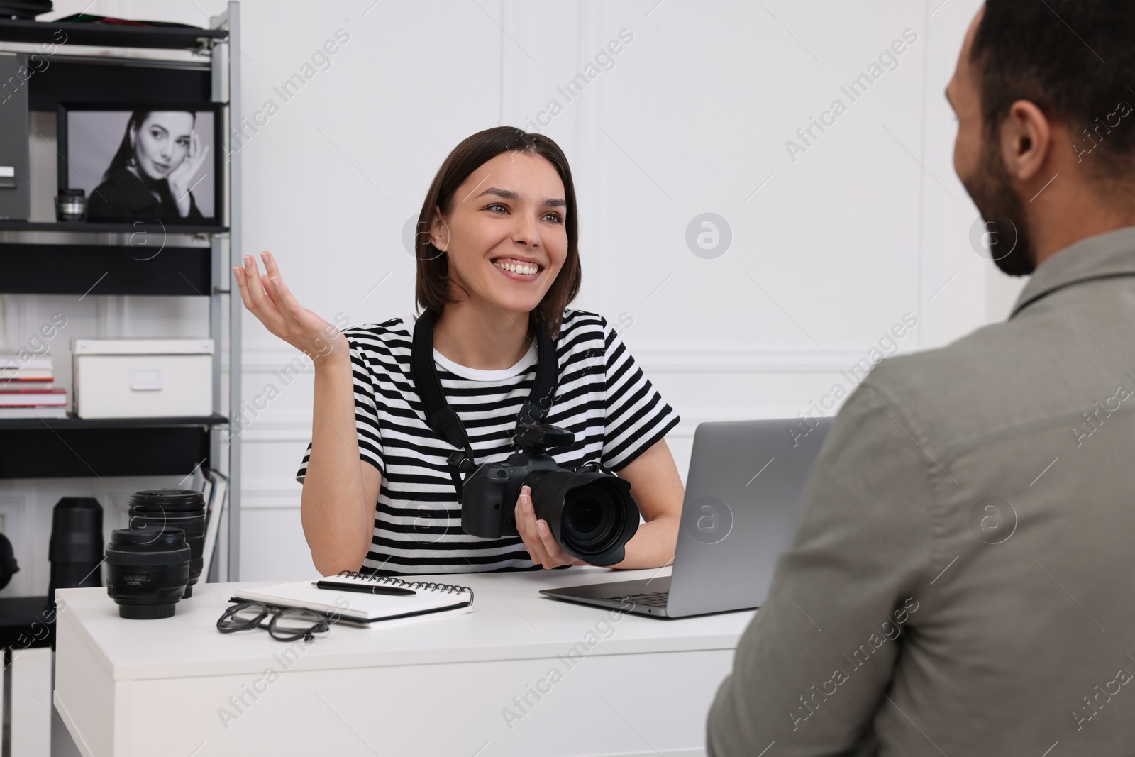 Photo of Young professional photographer holding camera while talking with man in modern photo studio