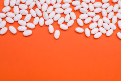 Many tasty dragee candies on orange background, flat lay. Space for text