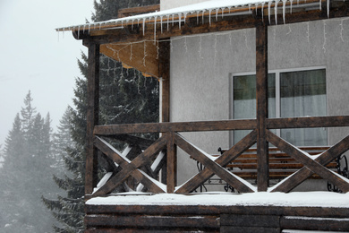 Wooden house with icicles on snowy day. Winter vacation