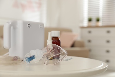 Photo of Modern nebulizer with face mask and medications on white table indoors. Inhalation equipment