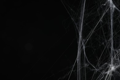 Photo of Creepy white cobweb on black background, closeup. Space for text