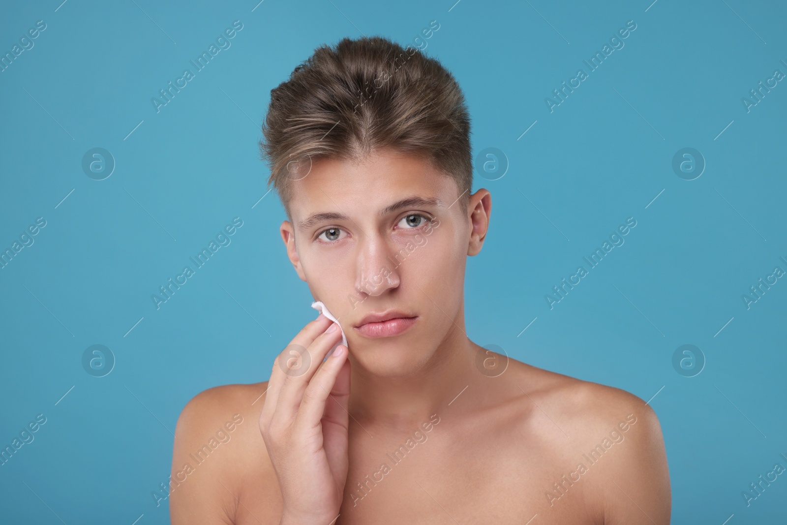 Photo of Handsome man cleaning face with cotton pad on light blue background