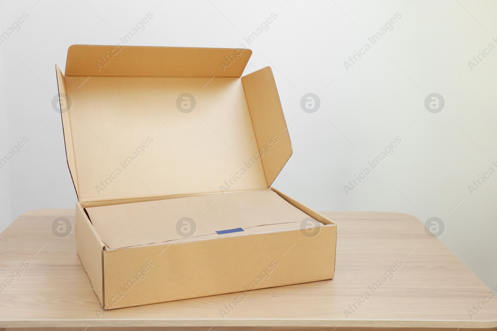 Photo of Open cardboard box with item wrapped in kraft paper on wooden table, space for text. Delivery service