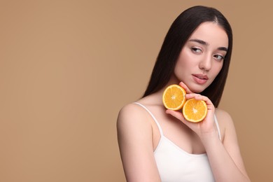 Beautiful young woman with pieces of orange on beige background. Space for text