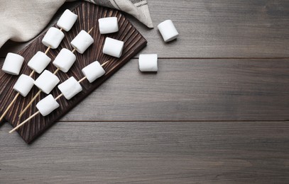 Photo of Sticks with marshmallows on wooden table, flat lay. Space for text