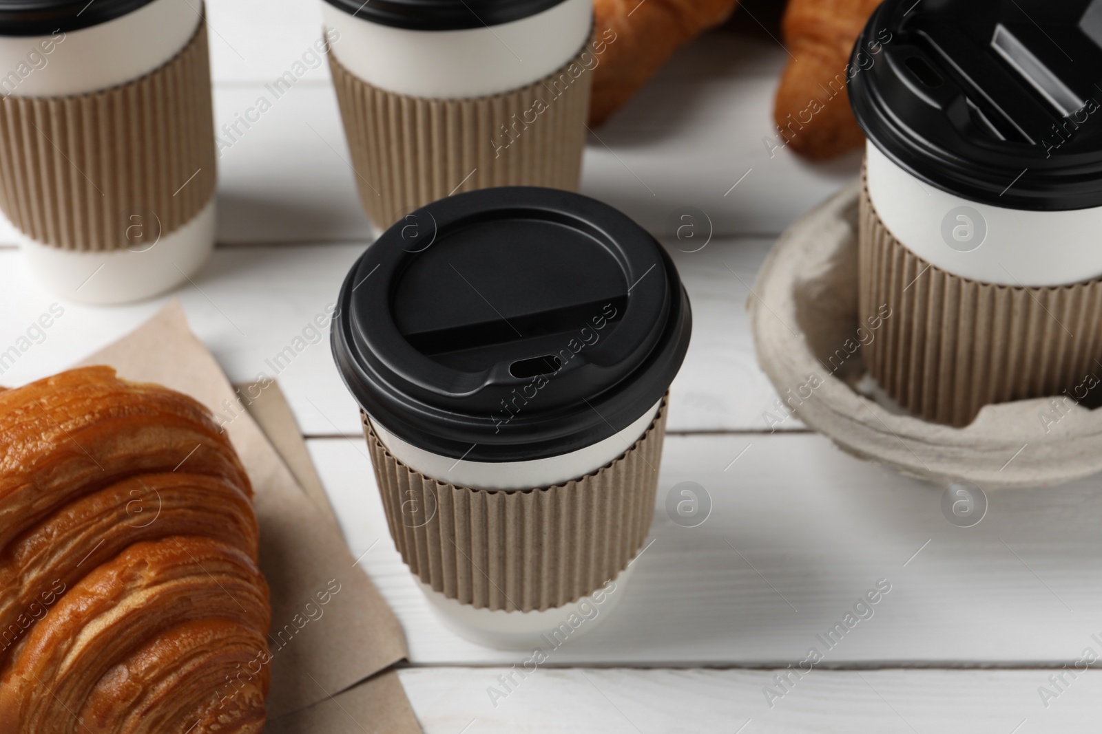 Photo of Coffee to go. Paper cups with tasty drink and croissants on white wooden table