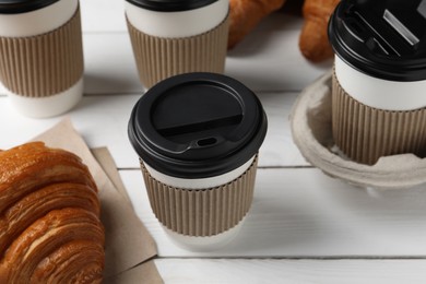 Photo of Coffee to go. Paper cups with tasty drink and croissants on white wooden table