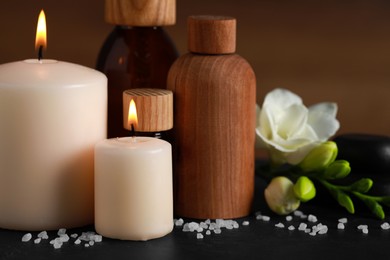 Photo of Beautiful spa composition with different care products and burning candles on black table, closeup