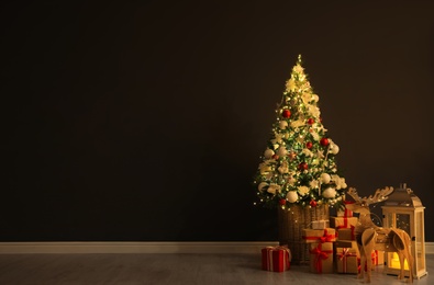Photo of Beautiful Christmas tree, festive decor and gift boxes near black wall indoors, space for text