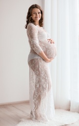 Young pregnant woman in elegant dress at home