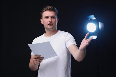 Casting call. Emotional man with script performing on black background