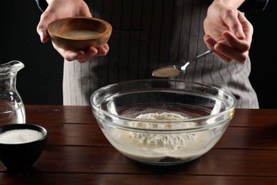 Photo of Making bread. Woman putting dry yeast into bowl at wooden table, closeup