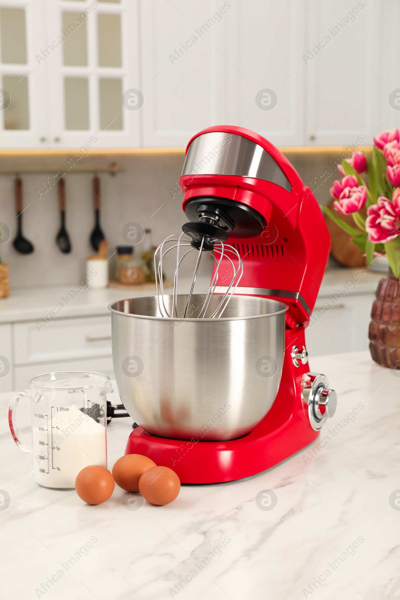 Photo of Modern red stand mixer, eggs and container with flour on white marble table in kitchen