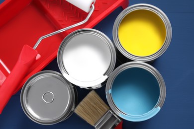 Photo of Cans of paints, brush, roller and tray on blue wooden table, flat lay