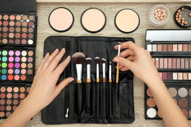 Photo of Professional makeup artist taking brush from organizer at wooden table, top view