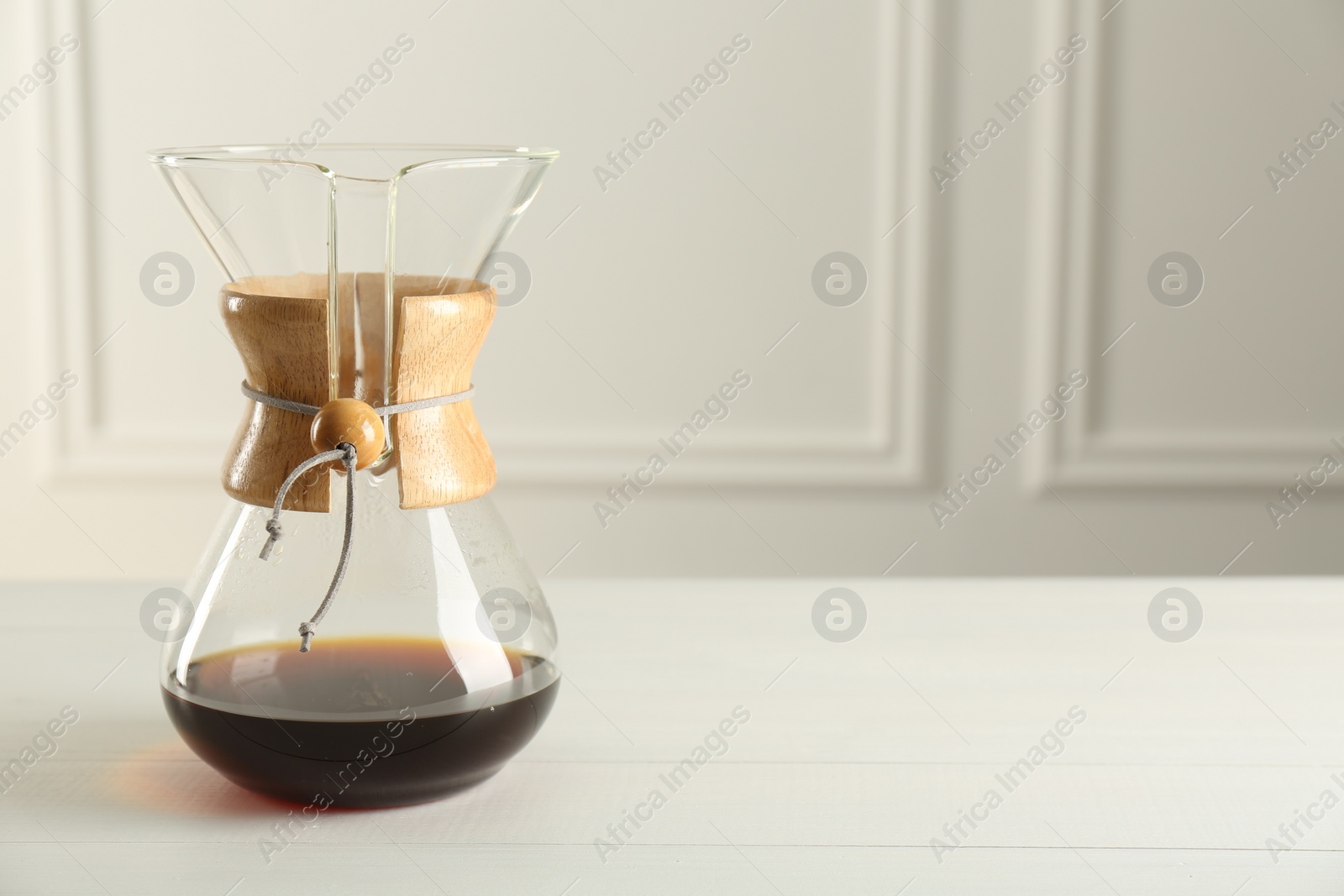 Photo of Glass chemex coffeemaker with coffee on white table, space for text