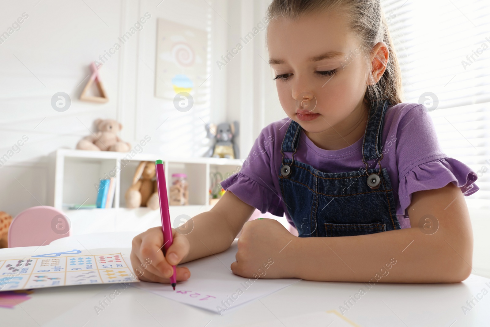 Photo of Little girl writing numbers in classroom at English lesson