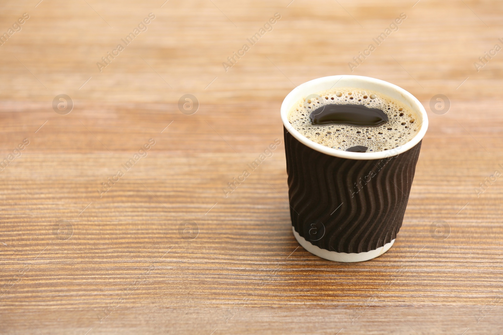 Photo of Cardboard cup of coffee on wooden table. Space for text