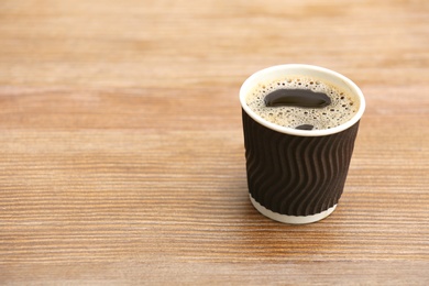 Cardboard cup of coffee on wooden table. Space for text