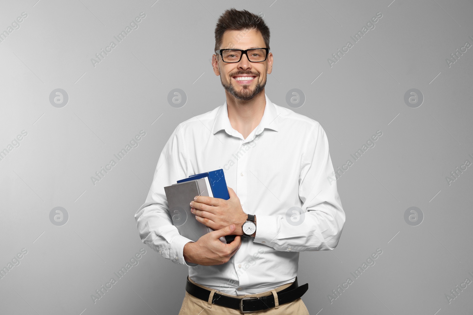 Photo of Happy teacher with glasses and books against beige background