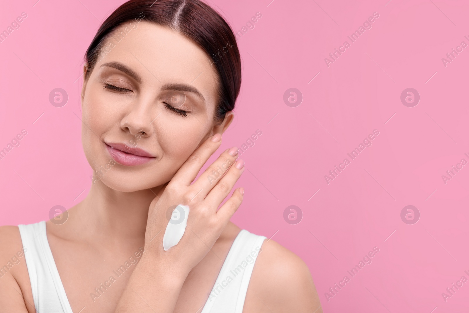 Photo of Beautiful woman with smear of body cream on her hand against pink background, space for text