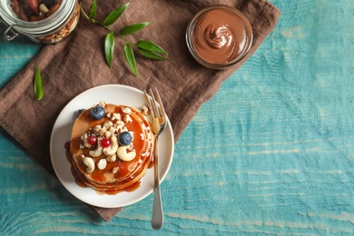 Tasty pancakes with berries, nuts and syrup on table, top view