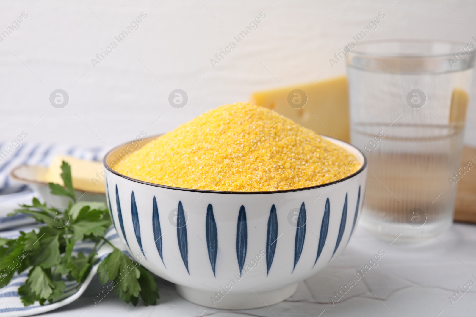 Photo of Raw cornmeal in bowl and parsley on light table, closeup