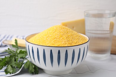 Raw cornmeal in bowl and parsley on light table, closeup