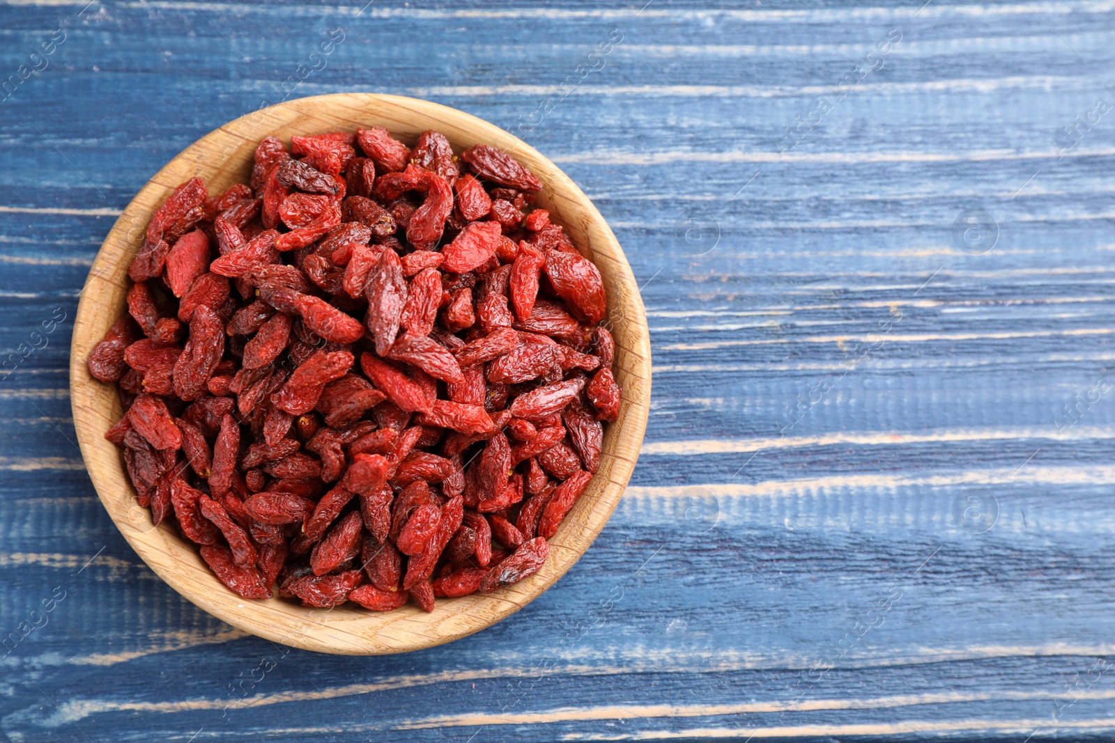 Photo of Dry goji berries on blue wooden table, top view. Space for text