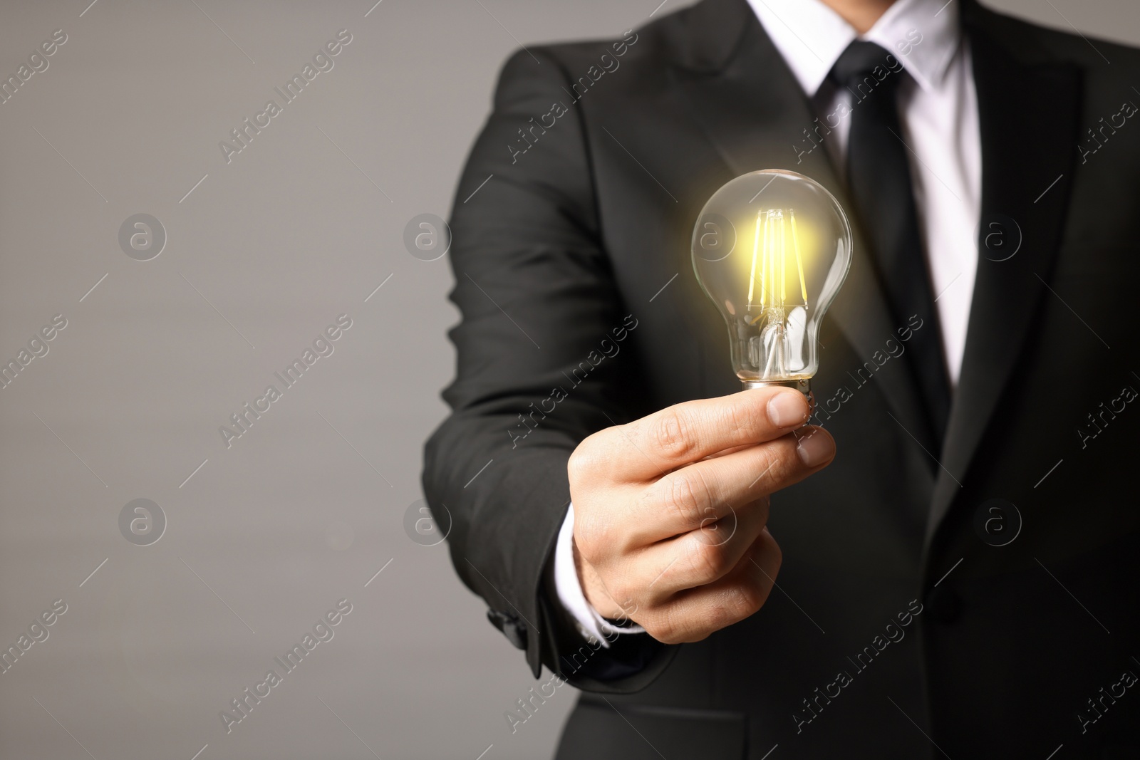 Photo of Glow up your ideas. Closeup view of businessman holding light bulb on grey background, space for text