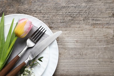 Stylish table setting with cutlery and flowers on wooden background, top view. Space for text